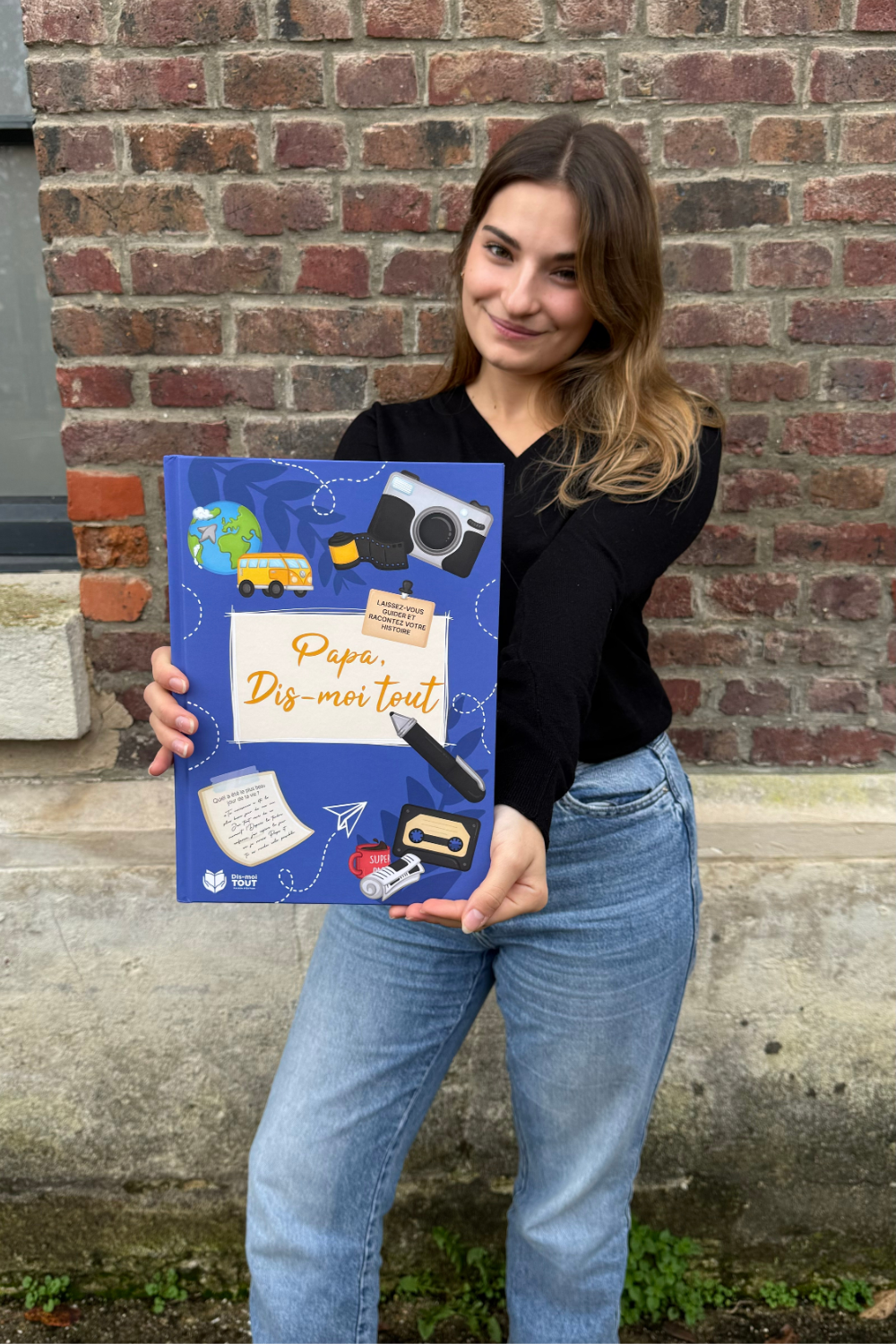 Une fille tient entre ses mains le livre Papa, Dis-moi tout pour nous le montrer