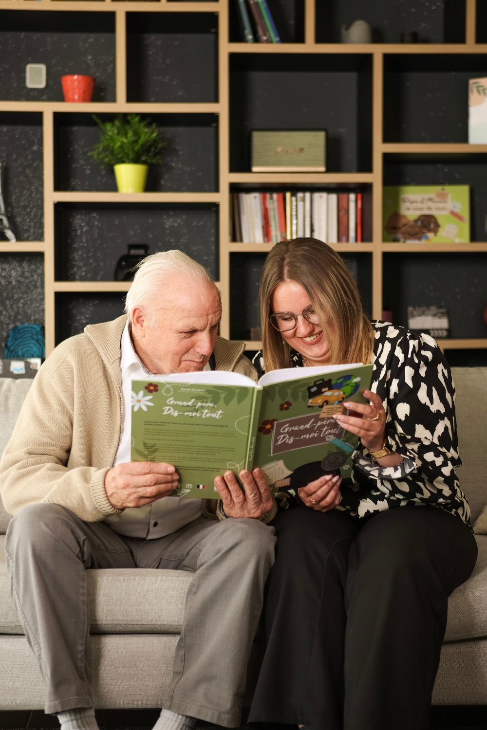 un grand-père et sa petite fille rient devant le livre grand-père, dis-moi tout