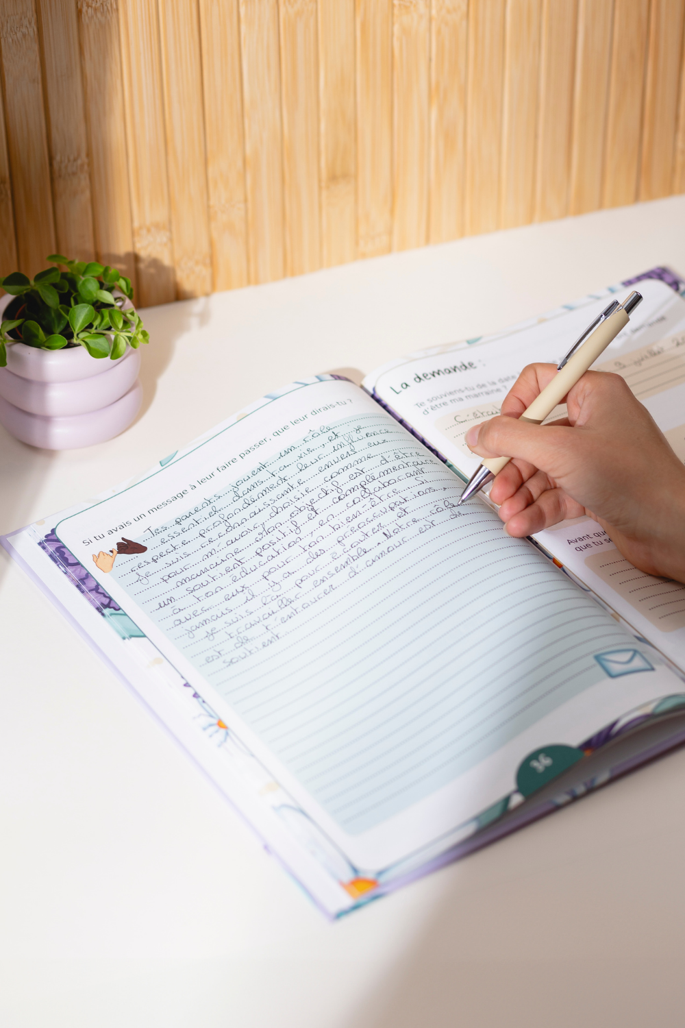 Photo du livre "Marraine, Dis-moi tout" ouvert avec une main qui est entrain d'écrire à l'intérieur