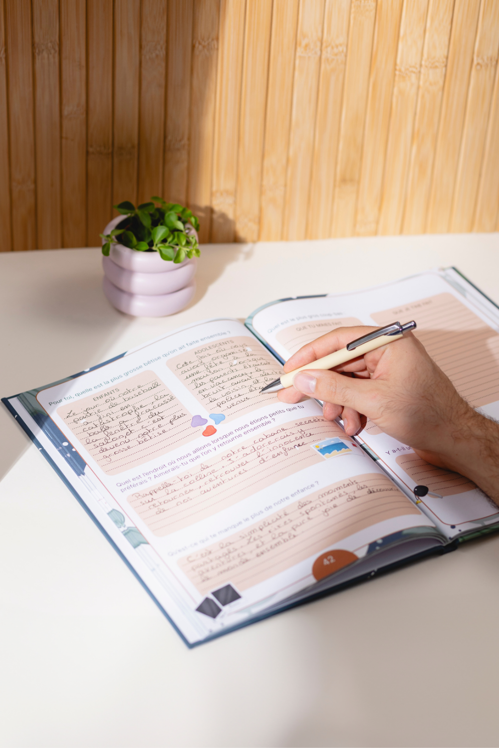 Le livre "Mon frère, Dis-moi tout" est ouvert sur une double page. Une personne est entrain d'écrire à l'intérieur