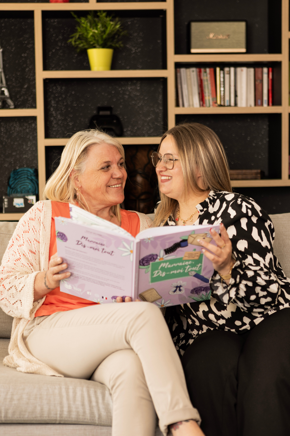 Deux femmes se regardent en souriant en tenant le livre "Marraine, Dis-moi tout" entre leurs mains